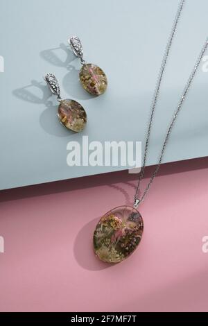 Boucles d'oreilles en résine et collier avec fleurs naturelles à l'intérieur sur bleu et sur fond rose Banque D'Images