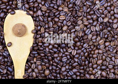 Gros plan, texture et arrière-plan de grains de café frais rôtis sur lesquels repose une cuillère en bois et une praline de truffe de chocolat sur le dessus Banque D'Images