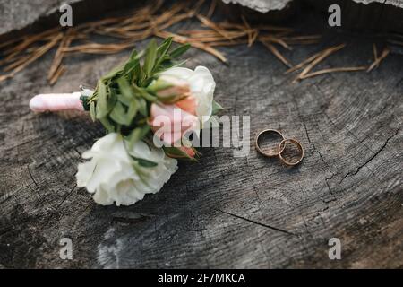 Anneaux de mariage et boutonnière sur fond de texture bois. Banque D'Images