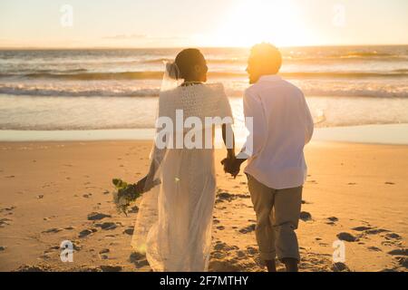 Couple afro-américain amoureux de se marier, marchant sur la plage pendant le coucher du soleil tenant les mains Banque D'Images