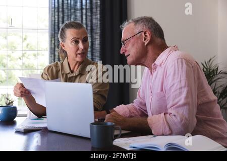 Couple âgé de race blanche dans la salle de séjour assis à la table en utilisant un ordinateur portable, en payant des factures et en parlant Banque D'Images