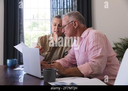 Couple âgé de race blanche dans la salle de séjour assis à la table en utilisant un ordinateur portable, en payant des factures et en parlant Banque D'Images