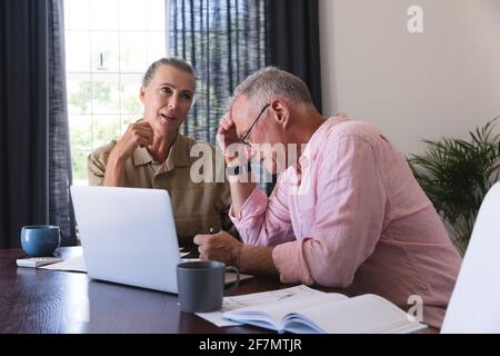 Inquiet caucasiens couple senior dans le salon à la table en utilisant l'ordinateur portable, faire de la paperasse et parler Banque D'Images