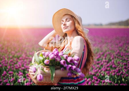 Belle femme à cheveux rouges vêtue d'une robe à rayures debout sur des champs de fleurs de tulipe colorés dans la région d'Amsterdam, Hollande. Paysage hollandais magique avec champ de tulipe. Concept Trevel et Spring. Banque D'Images