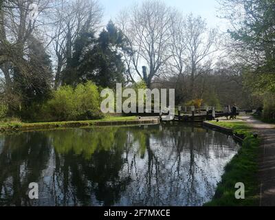 Couple assis à côté d'une écluse sur un canal tandis que la campagne environnante se reflète dans l'eau, Cassiobury Park Watford Angleterre. Banque D'Images