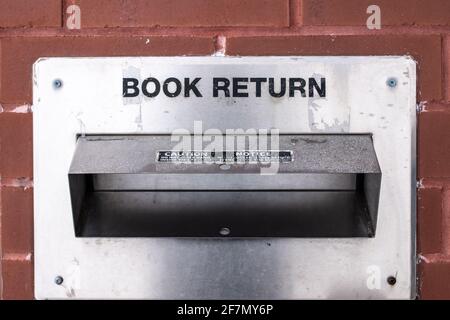 Un vieux conteneur de retour de livre en métal vieilli, abîmé dans un mur de briques dans le centre-ville de Londres. Lecture de livres pendant la pandémie de COVID-19, contrôle de gros volumes Banque D'Images