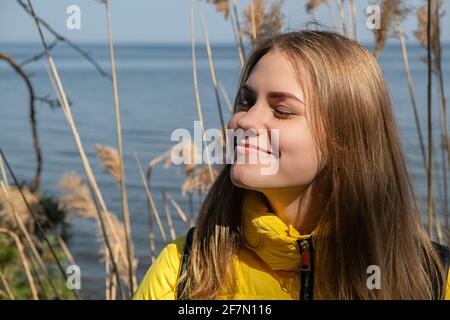 Portret, de la jeune femme souriante et heureuse, avec ses yeux fermés, profite du soleil et de l'air frais. Elle se tient contre le lac le jour chaud du printemps en jaune Banque D'Images