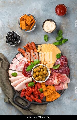 Les viandes coupées, les saucisses et les fromages de différents types sont coupés sur une planche sur fond gris. Carte de charcuterie. Vue de dessus, verticale. Banque D'Images