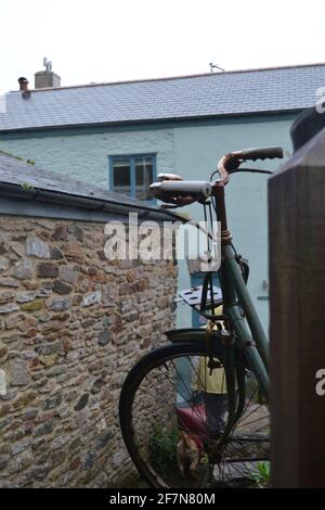 Un vieux vélo vert et rouillé a été soutenu dans l'arrière-cour d'un cottage traditionnel à l'ancienne sous la pluie Banque D'Images