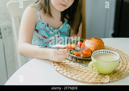 Fille prenant le petit déjeuner. Sandwich croissant avec fromage cottage, saumon, épinards, œuf poché, tasse de café. Petit déjeuner sain. Banque D'Images