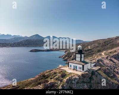 Vue aérienne du phare de Revellata sur un éperon rocheux à proximité Calvi dans la Balagne de Corse avec des sommets enneigés montagnes au loin Banque D'Images