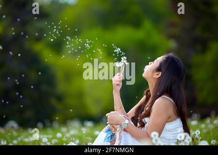 Vue latérale d'une philippine assise sur l'herbe et soufflant pissenlit en été sur le terrain Banque D'Images