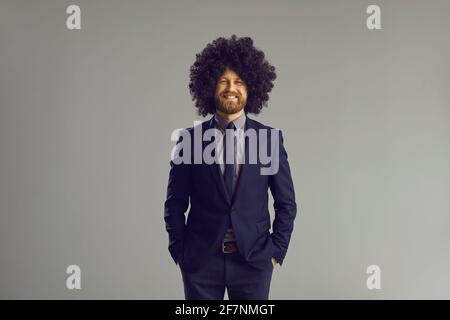 Un homme heureux dans un costume élégant et une perruque folle mains dans les poches et sourire Banque D'Images