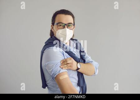 Homme asiatique vacciné en masque facial montrant du plâtre médical sur prise de vue studio arm Banque D'Images