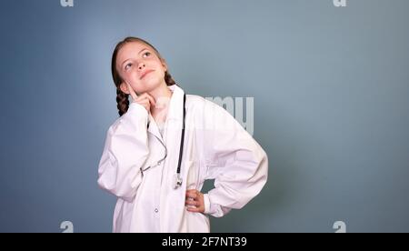 jolie fille avec deux tresses est habillée comme médecin et pose avec stéthoscope sur fond bleu, professions de concept Banque D'Images