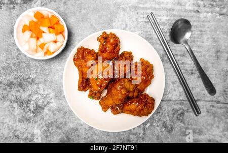 Vue de dessus poulet coréen épicé au friture surmontée de sésame blanc avec carottes marinées et plats d'accompagnement de radis marinés sur la table en béton gris, populaire s. Banque D'Images