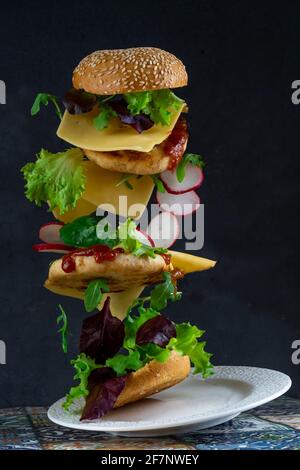 Tranches de hamburger à lever.Nourriture volante.Pain hamburger, double escalope de poulet avec fromage, laitue, arugula et radis.Viande, légumes et pain.Ingrédients sur fond noir. Banque D'Images