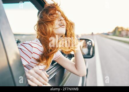 bonne femme aux cheveux rouges regarde par la fenêtre de la voiture et conduit sur la route, piste des vacances d'été Banque D'Images