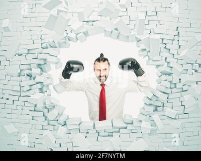 homme d'affaires avec des gants de boxe brise un mur de brique. concept de force et de détermination. Banque D'Images