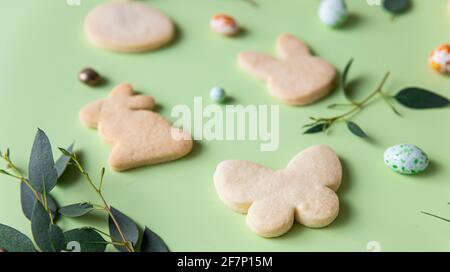 Biscuits de Pâques, œufs en forme de bonbons, eucalyptus, fleurs et œufs de caille sur fond vert pastel. Concept joyeuses Pâques. Gros plan. Mise au point sélective. Banque D'Images