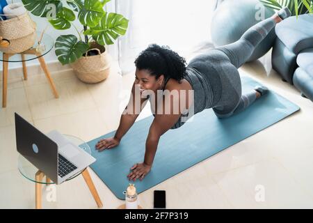 Jeune femme africaine curvy faisant pilates classe de forme physique virtuelle avec ordinateur portable à la maison - Sport bien-être personnes style de vie concept Banque D'Images