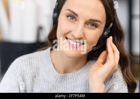 Femme de soutien en contact. Chat vidéo avec une jeune femme souriante portant un casque regarde la caméra, parle avec des clients ou des collègues à distance, une employée a participé à une réunion vidéo Banque D'Images