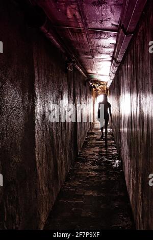 Silhouette d'une jeune femme à l'intérieur d'un chemin étroit et sombre, marchant contre la lumière au bout du tunnel, vu aux Philippines, en Asie Banque D'Images