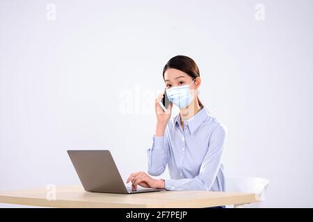 Une jeune femme avec un masque est au téléphone dans la vue latérale du bureau Banque D'Images