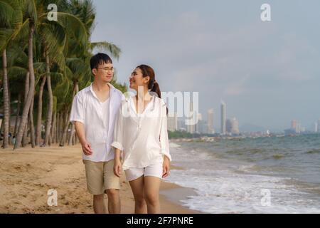 Le couple asiatique marche et s'embrasse sur une plage en bord de mer avec des cocotiers pendant ses vacances en été en Thaïlande. Banque D'Images