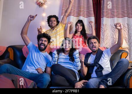 Un groupe de fans indiens de cricket crient et applaudissent pour soutenir l'équipe tout en regardant le sport à la télévision à la maison. Banque D'Images