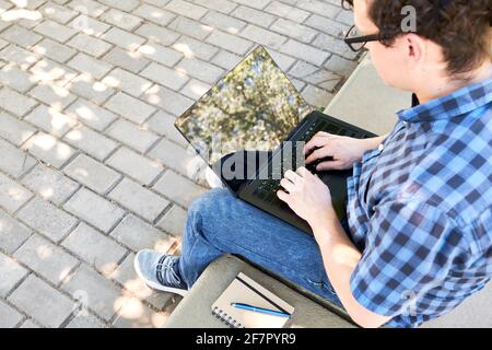 Jeune homme tapant sur un ordinateur portable à l'extérieur. Concept de nomade numérique, de travail ou d'étude en plein air. Banque D'Images