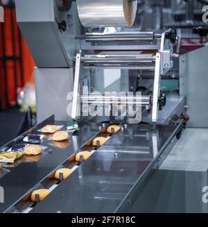 Gâteaux sur machine d'emballage à flux de film plastique dans la chaîne de production de boulangerie. Industrie alimentaire Banque D'Images