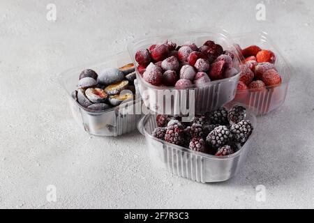 Baies congelées comme les cerises, les fraises, les prunes et les mûres dans les boîtes de stockage sur fond gris en béton Banque D'Images
