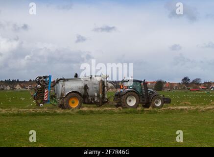 Tracteur avec réservoir de lisier et injecteur de lisier, en arrière-plan un village Banque D'Images