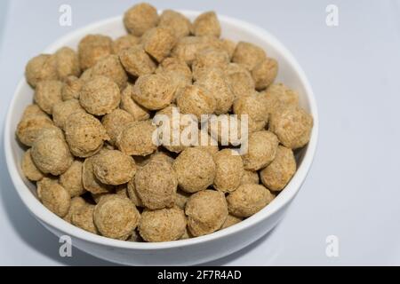 Un gros plan de nuggets de soja dans un bol à fond blanc. Les pépites de soja sont une source riche de protéines, particulièrement pour les végétaliens. Banque D'Images