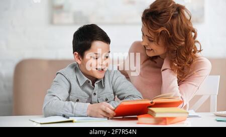 Un garçon positif lisant le livre près de la mère à la maison Banque D'Images