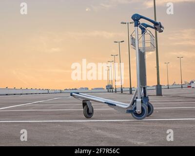 Chariot à bagages sur le pont vide du parc de l'aéroport pendant la crise corona devant le ciel orange Banque D'Images