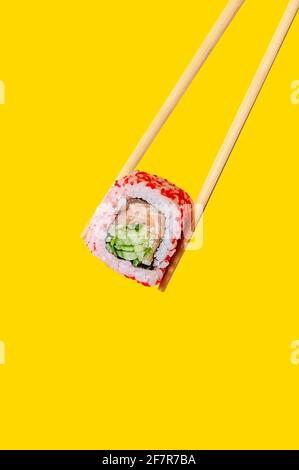 Gros plan California Roll avec du saumon et du concombre sur des baguettes sur fond jaune. Banque D'Images