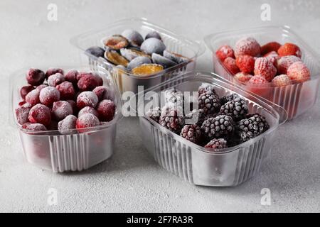 Baies congelées telles que cerises, fraises, prunes et mûres dans les boîtes de stockage sur fond gris clair Banque D'Images