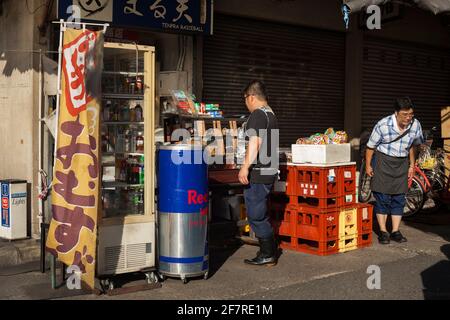 Vue horizontale de deux hommes, l'un d'eux prenant un arc, dans l'un des stands de snack du marché extérieur de Tsukiji à Tokyo (Jogai-Shijo), Tsukiji, Tokyo, Japon Banque D'Images