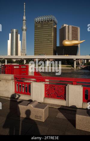 Vue sur les silhouettes de deux touristes sur le pont Azuma-Bashi au-dessus de la rivière Sumida avec le ciel de Tokyo et la flamme Asahi en arrière-plan, Asakusa Banque D'Images