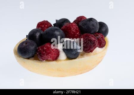 Œuf de chocolat blanc rempli de mousse de fruits de la passion décorée avec canneberges séchées et bleuets frais isolés sur blanc Banque D'Images