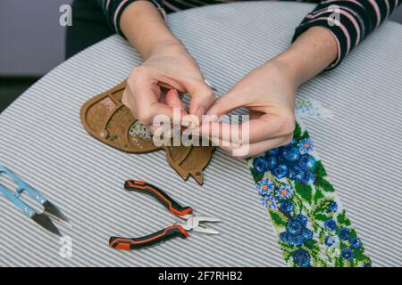 Tissage à partir de perles. Gros plan - les mains d'une femme sont en train de faire des perles sur un fil, faisant des bijoux. La femme aime tisser à partir de perles. Banque D'Images