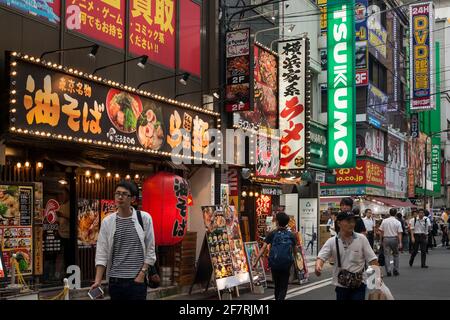 Vue horizontale de certaines personnes passant par une rangée de fast-foods et magasins de nombreux panneaux de néon colorés à Akihabara Electric Town, Akihabara, Tokyo Banque D'Images