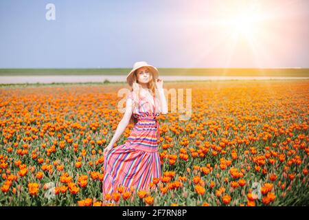 Belle femme à cheveux rouges vêtue d'une robe à rayures debout sur des champs de fleurs de tulipe colorés dans la région d'Amsterdam, Hollande. Paysage hollandais magique avec champ de tulipe. Concept Trevel et Spring. Banque D'Images