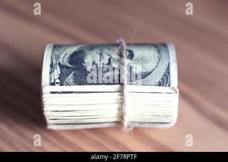 Les dollars AMÉRICAINS se sont mis à rouler et se sont resserrés avec un bracelet isolé table en bois Banque D'Images