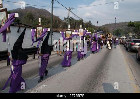 Les pénitents à capuche portent des croix lors de la procession Semana Santa à Antigua, Guatemala, une tradition solennelle de Carême reflétant la passion du Christ. Banque D'Images