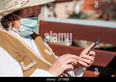Femme âgée isolée portant un masque médical, utilisant un téléphone portable. Banque D'Images