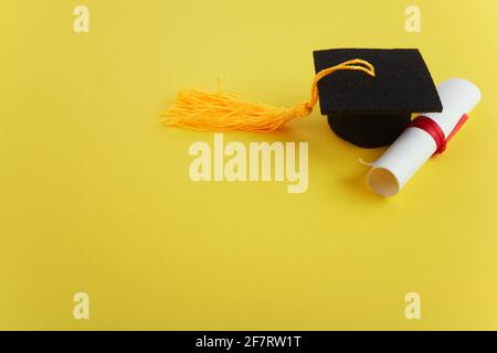 Chapeau universitaire avec diplôme sur fond jaune. Thème de la remise des diplômes Banque D'Images