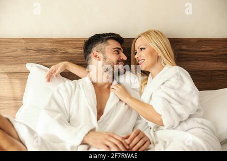 Faites des souvenirs dans une chambre d'hôtel, une douce touche d'amour. Un beau couple souriant, une jolie femme blonde et un bel homme, dans des peignoirs blancs enj Banque D'Images